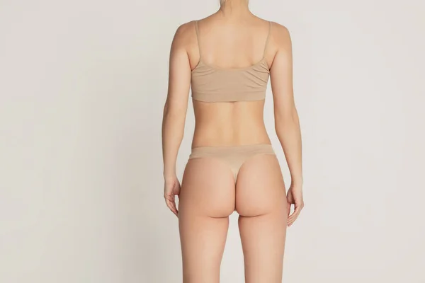 Bellissimo corpo femminile in biancheria intima di colore nudo su sfondo grigio. — Foto Stock