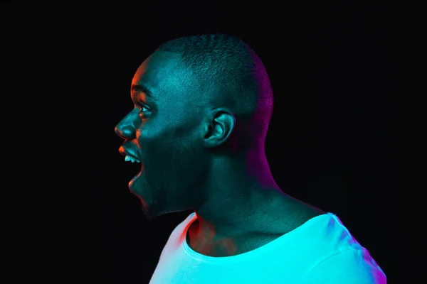 Young happy African-American man isolated on dark background in neon light — Stock Photo, Image