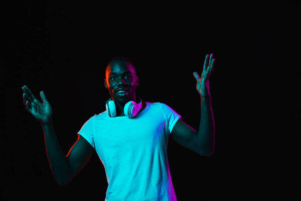 Happiness. Young African-American man in casual clothes isolated on dark background in multicolored neon light. Concept of human emotion, facial expression, youth culture. Copy space for ad.