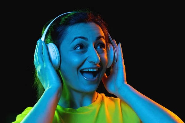 Jedna krásná žena ve sluchátkách izolované na tmavém pozadí v neonovém světle — Stock fotografie