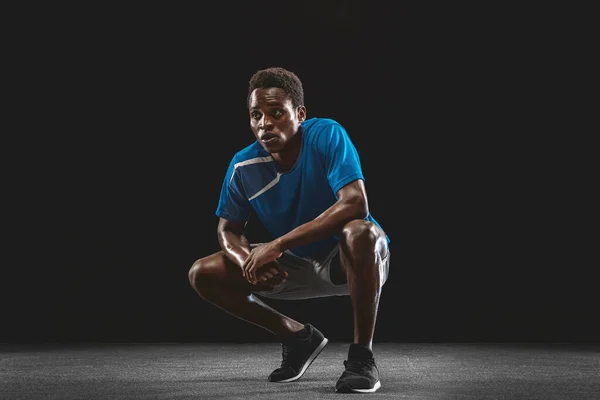 Portrait of young African man, athlete posing isolated over black background.