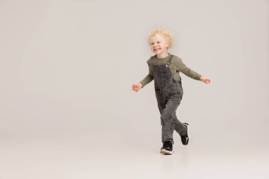 Kafkasyalı küçük albino çocuk gri stüdyo arka planında tek başına koşuyor..