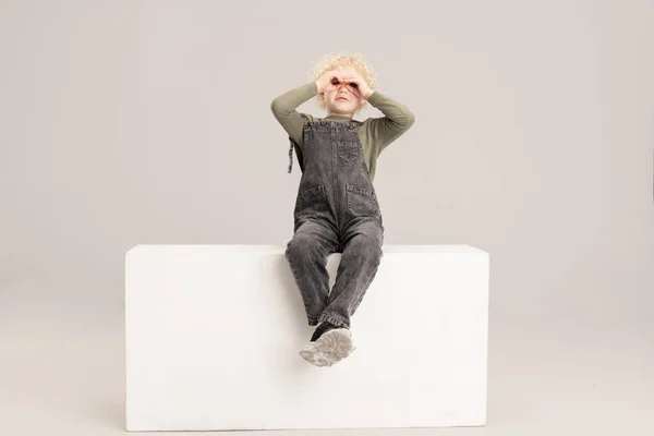 Jeden biały mały chłopiec siedzi na pudełku odizolowany nad szary studio tło. — Zdjęcie stockowe