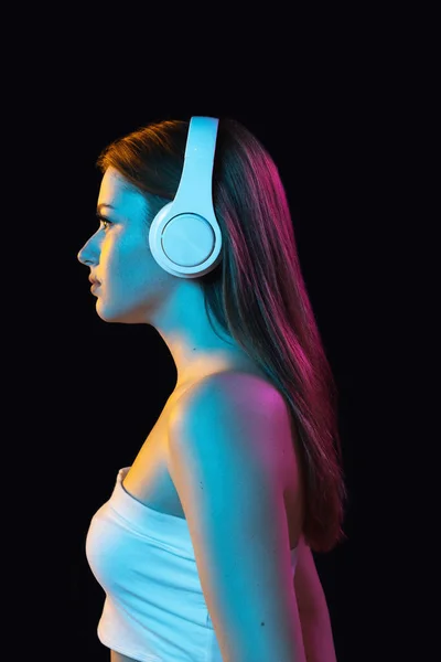 Portrait of young beautiful girl in headphones isolated over dark background. — Stock Photo, Image