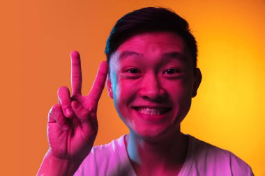 Yakın plan Asyalı genç adam, neon ışıklarıyla turuncu arkaplan üzerinde izole edilmiş..