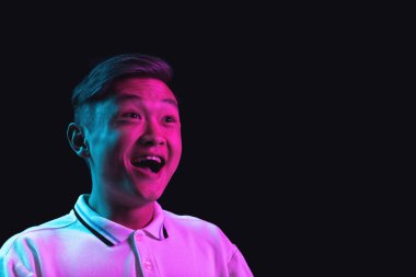 Asyalı genç adam portresi karanlık stüdyo arka planında neon ışığı altında izole edilmiş..