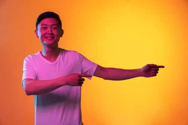 Retrato de un joven asiático aislado sobre fondo amarillo anaranjado en luz de neón. — Foto de Stock