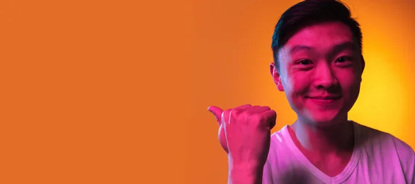 Close-up Asian young man isolated over gradient orange yellow background in neon light. — Stock Photo, Image
