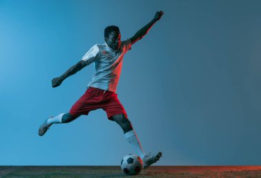 Neon ışıklarıyla mavi arka planda izole bir şekilde zıplayan Afrikalı futbolcu portresi