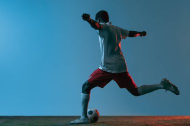 Genç Afrikalı futbolcu neon ışıkta mavi arka planda yalnız poz veriyor. Arka görünüm