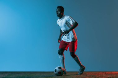 Neon ışıklarıyla mavi arka planda izole bir şekilde zıplayan Afrikalı futbolcu portresi