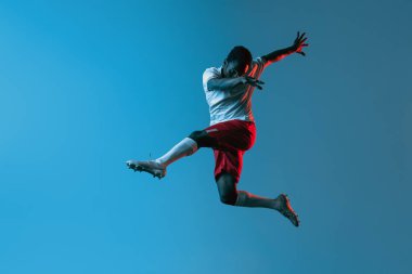 Bir Afrikalı futbolcu mavi arka planda neon ışıkta izole bir şekilde zıplıyor.