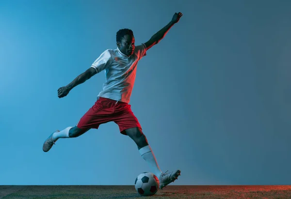 Πορτρέτο Αφρικής ποδοσφαιριστής άλμα απομονωμένο σε μπλε φόντο στο φως νέον — Φωτογραφία Αρχείου