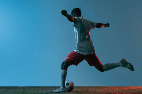 Νεαρός Αφρικανός ποδοσφαιριστής ποζάρει απομονωμένος σε μπλε φόντο υπό νέον φως. Πίσω όψη — Φωτογραφία Αρχείου