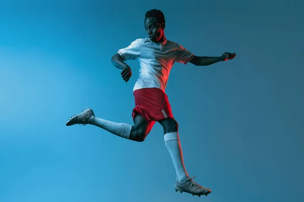 Κοντινό πλάνο Αφρικής ποδοσφαιριστής άλμα απομονωμένο σε μπλε φόντο σε νέον φως — Φωτογραφία Αρχείου