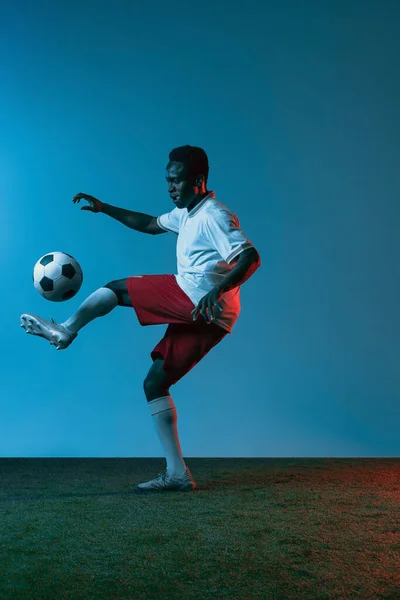 Ritratto calciatore africano che salta isolato su sfondo blu in luce al neon — Foto Stock