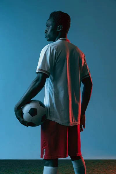 Close-up African man football player isolated on blue background in neon light