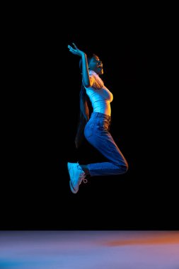 Genç mutlu, neşe dolu Afrikalı kız karanlık arka planda karışık neon ışıklarda tek başına zıplıyor..