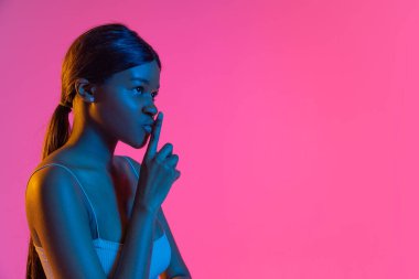Pembe arka planda, neon ışıkta izole edilmiş güzel Afrikalı bir kızın portresi. Yan görünüm