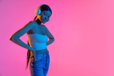 Pembe arka planda, neon ışıkta izole edilmiş güzel Afrikalı bir kızın portresi. Yan görünüm