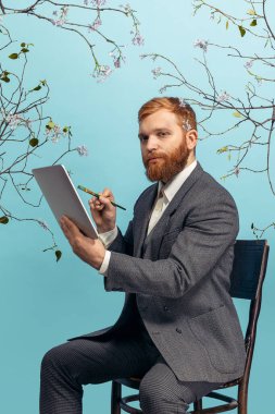 Genç kızıl saçlı ve sakallı bir adamın portresi. Ünlü bir sanatçıymış gibi davranıyor. Mavi çiçekli arka planda izole edilmiş.