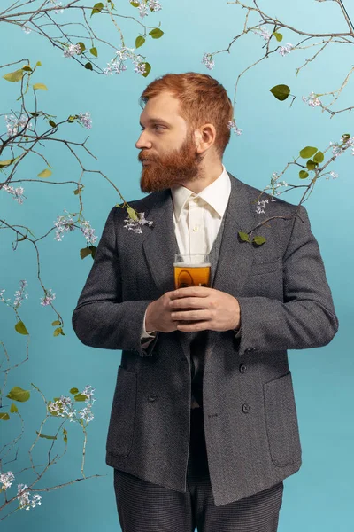 Portrait de jeune homme à tête rouge et barbu avec verre de bière isolé sur fond bleu floral — Photo