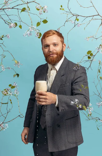 Portrait de jeune homme à tête rouge et barbu avec verre de bière isolé sur fond bleu floral — Photo