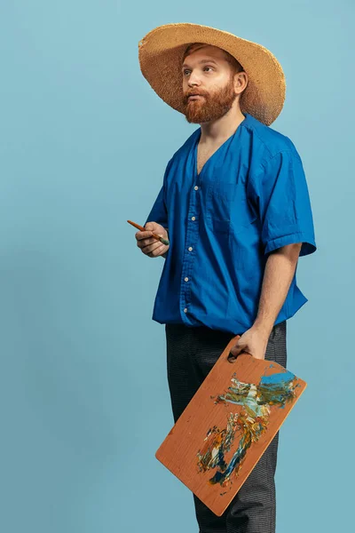 Jeune homme à la tête rouge et barbu en chapeau de paille se tenant isolé sur fond bleu. Comparaison Eras — Photo