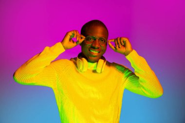 Gülümseyen mutlu Afrikalı yakışıklı adam, mor renkli neon arka planda soyutlanmış poz veriyor..