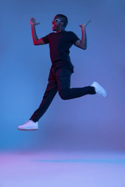 Genç Afrikalı yakışıklı adam, karanlık arka planda karışık neon ışıkta izole bir şekilde zıplıyor. El ilanı