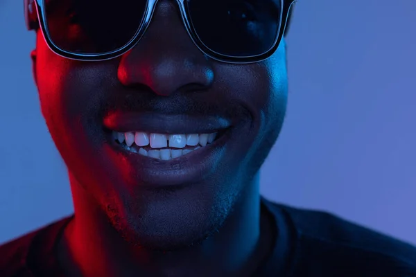 Retrato recortado de jovem homem bonito Africano posando isolado sobre fundo escuro em luz de néon mista. — Fotografia de Stock