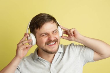 Sarı arka planda izole edilmiş, gülümseyen, kulaklıklı, beyaz bir adam. Yüz ifadeleri, insan duyguları kavramı.