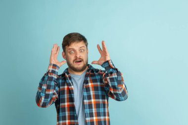 Şok, stres. Açık mavi arka planda izole edilmiş günlük giysiler içinde beyaz sakallı genç bir adam..