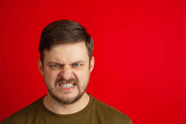 Angry young Caucasian man isolated on bright red studio background. Concept of facial expressions, human emotions. — Stock Photo, Image