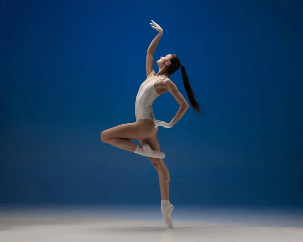 Graceful jong mooi meisje, vrouwelijke balletdanseres dansen geïsoleerd over blauwe achtergrond. — Stockfoto