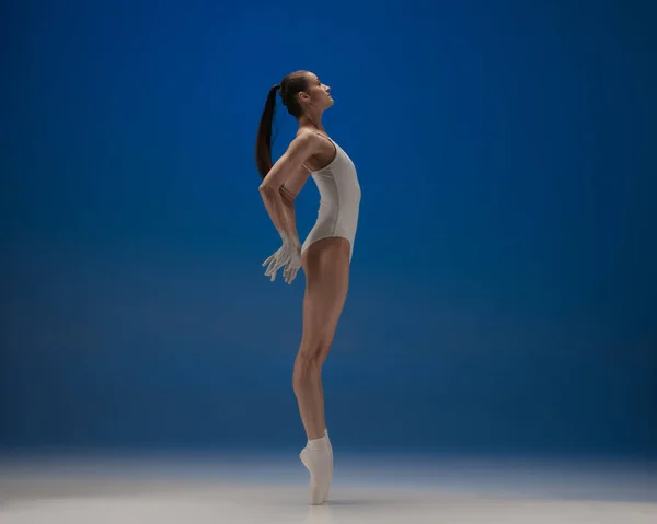 Nas pontas dos pés. Jovem bela bailarina em ação isolada sobre fundo azul. — Fotografia de Stock