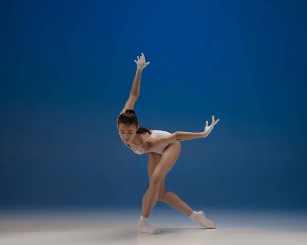 Jonge mooie ballerina in actie geïsoleerd over blauwe achtergrond. Concept van schoonheid, kunst, show, theater. — Stockfoto