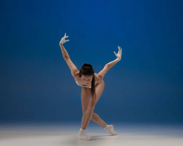 Jeune belle ballerine en action isolée sur fond bleu. Concept de beauté, art, spectacle, théâtre. — Photo
