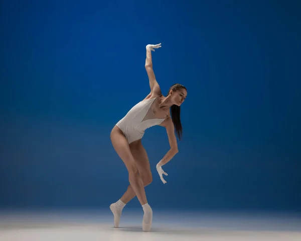 Jonge mooie ballerina in actie geïsoleerd over blauwe achtergrond. Concept van schoonheid, kunst, show, theater. — Stockfoto