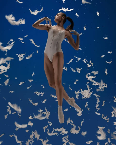Szárnyalj, mint egy madár. Egy fiatal női balett táncos repül elszigetelt kék háttér fehér tollak. — Stock Fotó