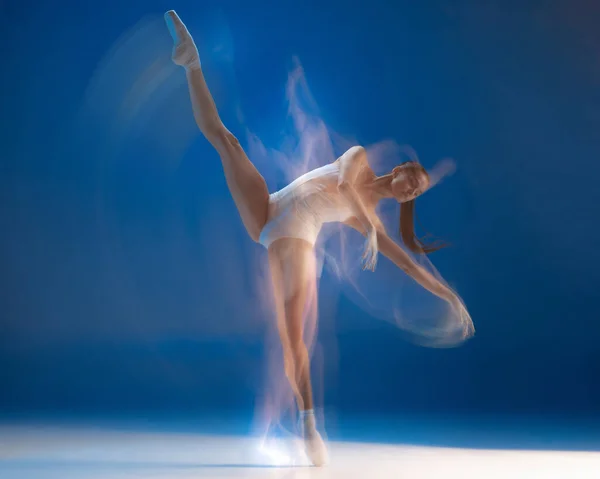 Na czubkach palców. Młoda piękna balerina w akcji odizolowana na niebieskim tle. — Zdjęcie stockowe