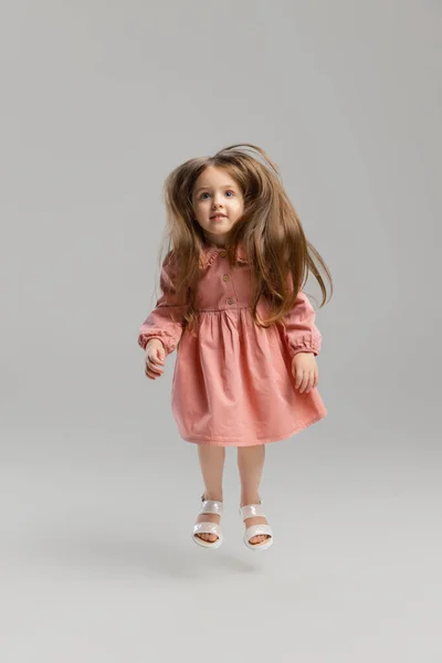 Портрет маленькой белой милой девушки, позирующей на фоне серой студии. — стоковое фото