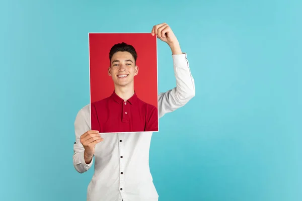 Egy fiatal fiú, fehér inges tinédzser, kezében a portréjával, elszigetelve a világoskék háttérben. Maszk — Stock Fotó
