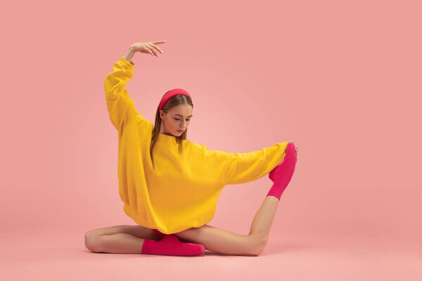 Portrait of young beautiful girl, female ballet dancer training isolated over pink background.