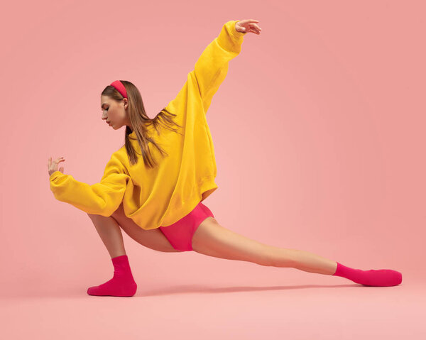 Flexible young beautiful girl, female ballet dancer training isolated over pink background.