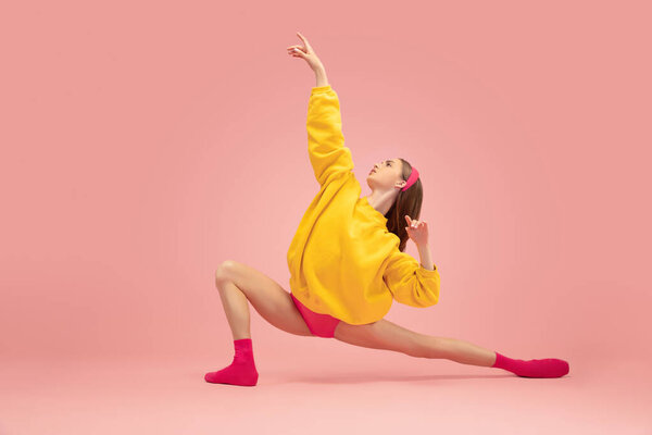 Flexible young beautiful girl, female ballet dancer training isolated over pink background.