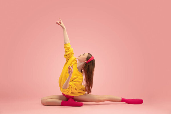 Flexible young beautiful girl, female ballet dancer training isolated over pink background.