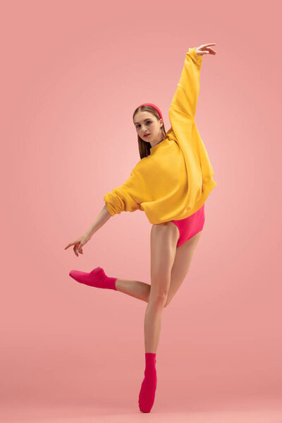 Flexible young beautiful girl, female ballet dancer training isolated over pink background.