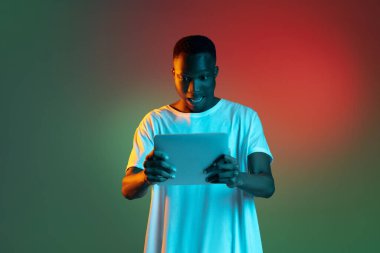 Genç Afrikalı adam, arka planda neon ışığı altında tablet kullanıyor..