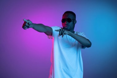 Güneş gözlüklü genç Afrikalı adam, arka planda neon ışıkta poz veriyor. Duyguların kavramı, yüz ifadesi.